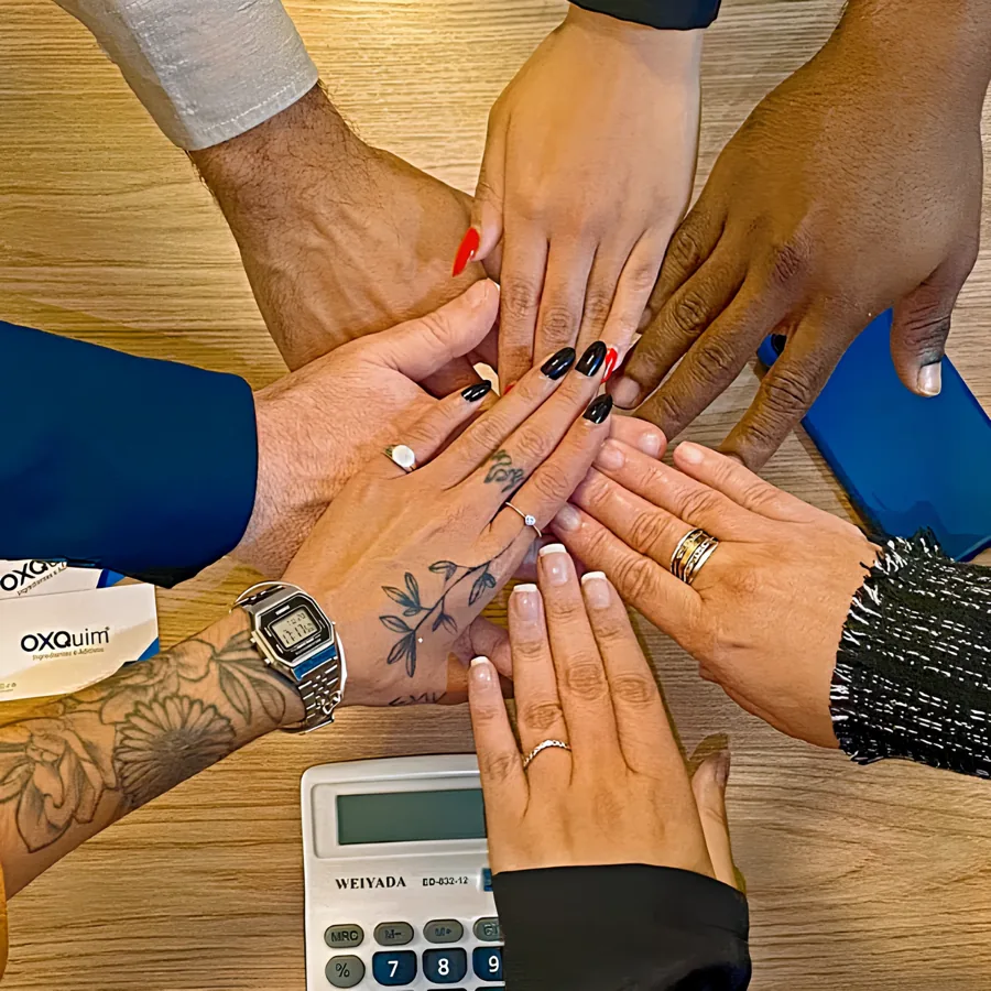 Mãos da equipe OXQuim unidas sobre a mesa de trabalho, representando relação de longo prazo e presença B2B